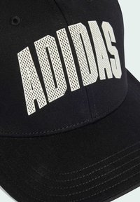 Gorra de béisbol negra con el prominente texto perforado en blanco "ADIDAS". Diseño estructurado con un visor curvado y tela de algodón para dar textura.