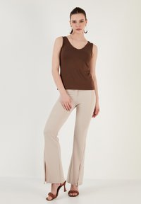 Brown sleeveless top with a V-neck paired with beige flared pants featuring side slits. Model wears brown strappy heels.