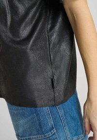 Top senza maniche nera con texture abbinato a jeans in denim blu, focalizzandosi sul dettaglio della cucitura laterale e su un braccio che pende naturalmente.