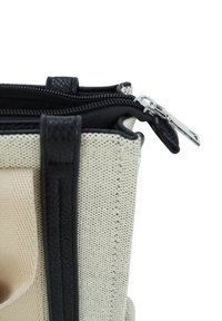 Beige en zwart getextureerde stoffen tas met dubbele compartimenten, zwarte leren afwerking en gedeeltelijk open zilveren ritsen.