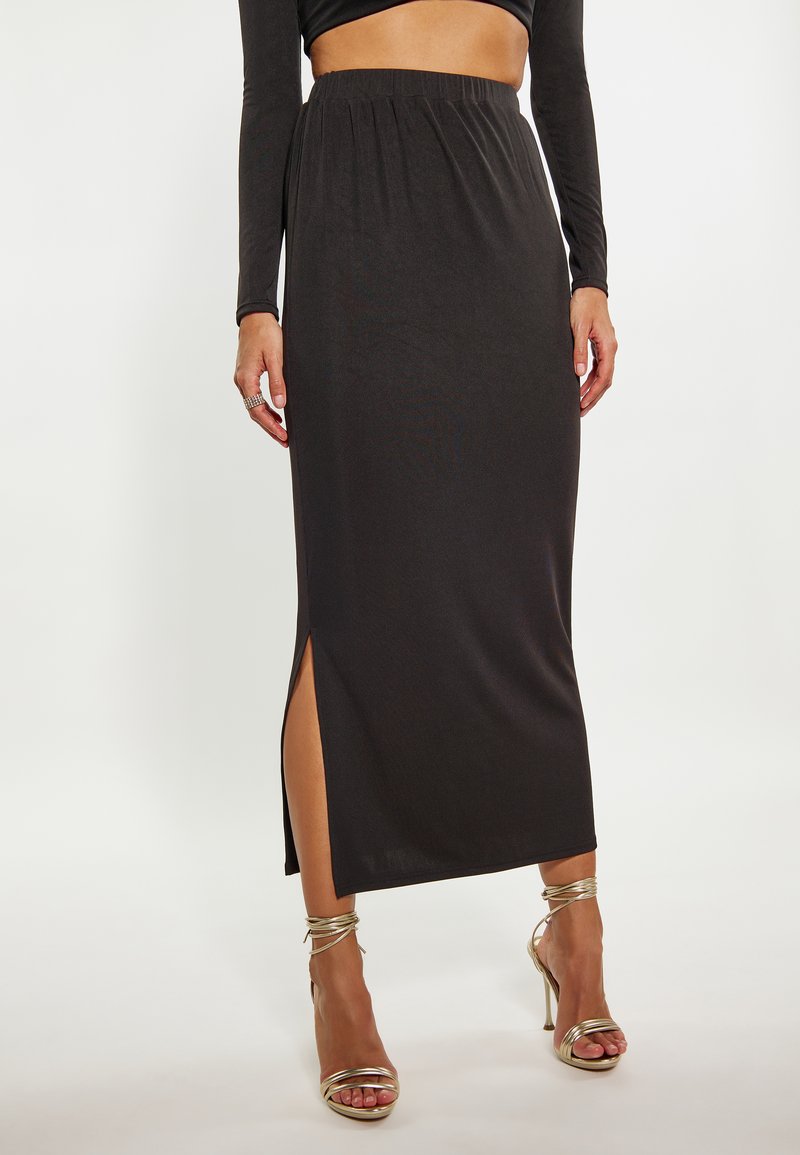 Zwarte geribbelde midi-rok met zijwaartse split, elastische tailleband, gecombineerd met gouden gespsandalen met hoge hakken. Glad textuur, aansluitend ontwerp.