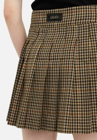 Gonna a pieghe a quadri marrone e blu navy con etichetta nera LIU JO sulla vita. Presenta un tessuto texture e un design strutturato.