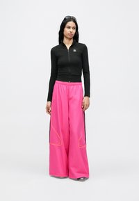 Fekete, cipzáros, hosszú ujjú felső, testhezálló szabással; laza, rózsaszín, bőszárú nadrágok fekete oldalsávokkal és sárga varrással díszítve.