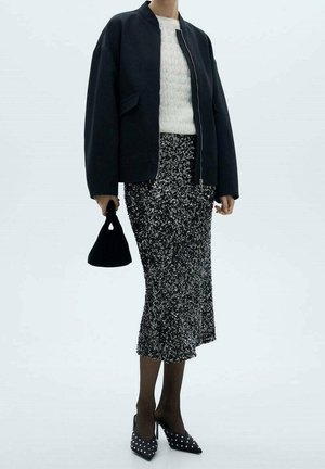 Zwarte bomberjack, crèmekleurige, getextureerde gebreide trui, zilveren paillettenrok, zwarte handtas en pumps met spits toelopende neus en witte studs.