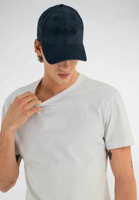 Cappello blu scuro con logo "GAS" in rilievo, abbinato a una maglietta grigia chiara a maniche corte con un piccolo logo in rilievo sul petto.