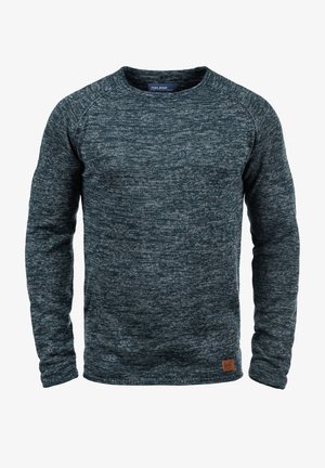 Pull en maille bleu marine avec un col rond et des manches longues. Présente un motif texturé et une petite étiquette en cuir de marque sur l'ourlet.