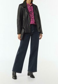 Giacca di pelle nera con cerniere argentate, blusa floreale rosa, jeans a gamba larga scuri e stivaletti con tacco a blocco neri. Design semplice e strutturato.