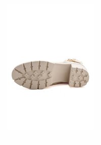 Suela de bota de goma beige con un relieve texturizado, que presenta múltiples ranuras para mejorar el agarre. El diseño incluye bordes reforzados y un perfil plano.