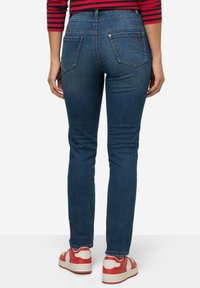 Kapeekit siniset farkut, joissa on keskipitkä vyötärö, kaksi takataskua ja hillitty haalistuminen. Yhdistetty punavalkoisiin tennareihin.