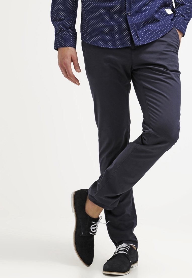 Navy Slim-Fit-Hosen aus einem glatten Stoff, kombiniert mit schwarzen Wildlederschuhen mit weißen Schnürsenkeln und einer hellen Sohle.