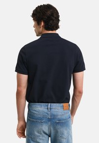 Námornícko modré polo tričko s krátkymi rukávmi a klasickým golierom, spárované s svetlomodrými džínsy z denimu s hnedou koženou nášivkou na páse.