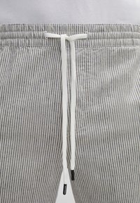Gestreifte, leichte Baumwollshorts in Grau und Weiß, mit einem elastischen Taillenbund und einem weißen Kordelzug mit schwarzen Spitzen.