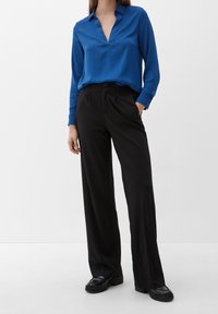 Blusa blu a maniche lunghe con scollatura a V, abbinata a pantaloni larghi a vita alta neri e scarpe con plateau nere.