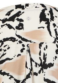 Weiße Bluse mit einem abstrakten schwarz-beigen Muster, einem Knopfdetail auf der Rückseite und einem Faltenwurf für zusätzlichen Fall.