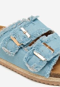 Sandaña de tejido azul claro desgastado que presenta dos correas ajustables con hebillas y una suela natural envuelta en yute con una base marrón texturizada.