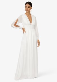 Robe blanche à manches longues avec un décolleté profond en V, des manches transparentes et une taille froncée. Fabriquée en tissu léger, elle présente une jupe fluide.
