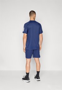 Tumed sportlik särk lühikeste varrukatega ja valgete detailidega, kombineeritud tumedate lühikeste pükstega. Valmistatud kergetest materjalidest. Mustad spordijalatsid valgete talladega.
