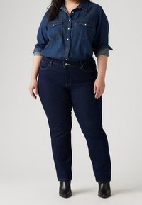 Mörkblå denimskjorta med uppkavlade ärmar, två bröstfickor och knäppning med knappar. Kombinerad med mörkblå jeans och svarta ankelstövlar.