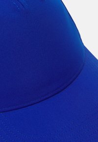 Boné azul feito de tecido liso, apresentando uma coroa arredondada e uma aba curvada. Inclui costuras cosidas e um design sem emendas.