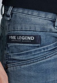 Džíny z denimu ve středně modrém odstínu s texturovaným povrchem. Mají tmavý látkový nášivku s nápisem "PME LEGEND AMERICAN CLASSIC."