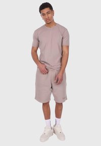 Lysebrun bomulds-t-shirt med korte ærmer, parret med matchende lysebrune shorts. Båret med hvide sneakers og ankelsokker.