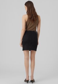 Jupe en denim noir avec une coupe ajustée, poches arrière, et d'une longueur mi-cuisse, assortie à un débardeur marron à côtes et des talons noirs.