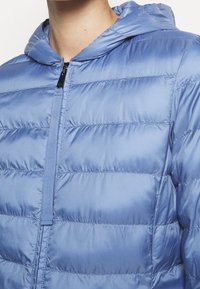 Jasnoniebieska kurtka puchowa z kapturem, z zamkiem z przodu i przeszytymi poziomymi panelami dla ocieplenia i faktury.