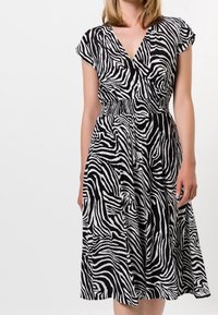 Vestido de estampado de cebra en blanco y negro, con escote en V, mangas cortas y cintura elástica. Falda hasta la rodilla con textura de tela fluida.