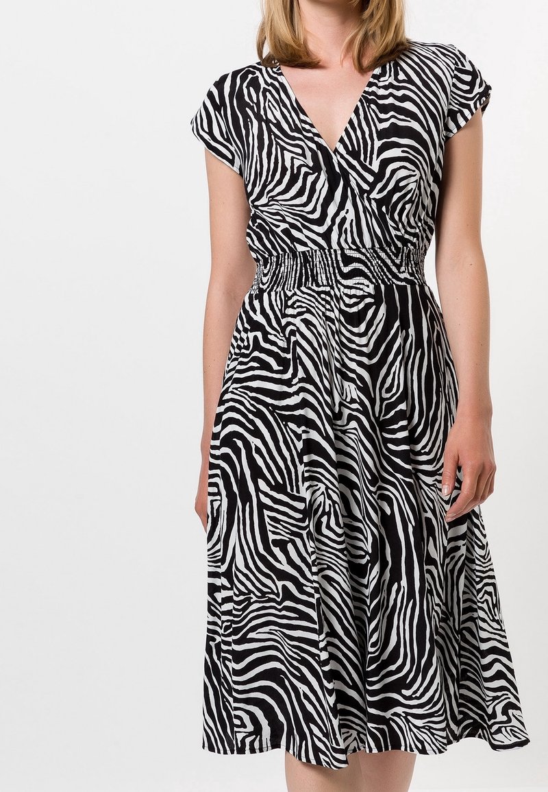 Vestido de estampado de cebra en blanco y negro, con escote en V, mangas cortas y cintura elástica. Falda hasta la rodilla con textura de tela fluida.