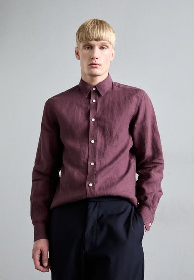 Camisa de manga larga color burdeos en tejido texturizado con cuello tipo polo y botones blancos, combinada con pantalones oscuros, llevada por un modelo.
