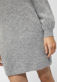 Abito grigio lavorato a maglia con finitura testurizzata, maniche lunghe e orlo a coste. Mano visibile appoggiata sull'abito, che mostra una finitura naturale delle unghie.