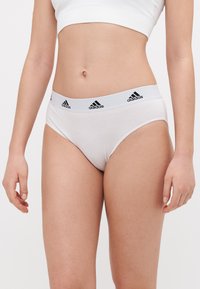 Bílé bavlněné kalhotky ve stylu bikiny s černým logem adidas na měkkém, elastickém pásku; hladká textura a klasický střih.