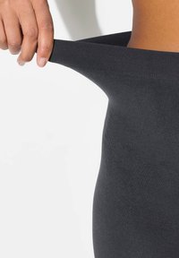 Leggings neri elasticizzati tenuti tra le dita, che mostrano una superficie liscia e una vita elasticizzata. Primo piano che cattura la flessibilità del tessuto.