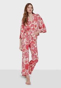 Conjunto de dos piezas con estampado floral rojo que presenta una blusa de estilo envolvente con mangas anchas y pantalones de corte holgado. Hecho de tela liviana.