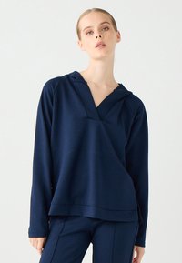 Dunkelblaues Kapuzenshirt mit V-Ausschnitt, langen Ärmeln und entspannter Passform. Hergestellt aus weichem Stoff mit glatter Textur, verfügt es über minimal sichtbare Nähte.