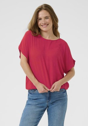 Blusa fucsia a maniche corte e vestibilità ampia, con texture morbida, scollo rotondo e arricciature all'orlo, abbinata a jeans in denim blu.