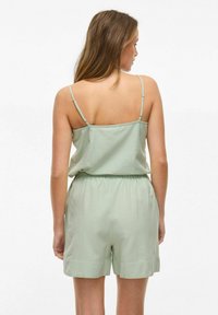 Mono sin mangas de color verde claro, con tirantes delgados, cintura elástica y pantalones cortos. Tejido suave con un ajuste relajado. Diseño simple y minimalista.