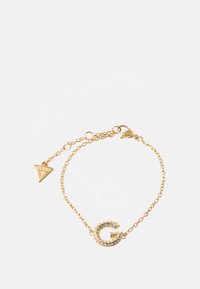 Gullkjedetarmbånd med et bokstav 'G'-anheng prydet med klare rhinestones og en trekantet 'GUESS'-tag. Glatt tekstur og slank design.