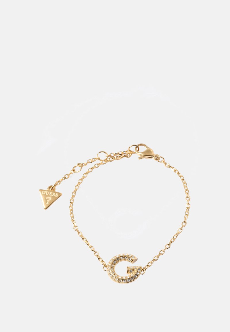 Gullkjedetarmbånd med et bokstav 'G'-anheng prydet med klare rhinestones og en trekantet 'GUESS'-tag. Glatt tekstur og slank design.