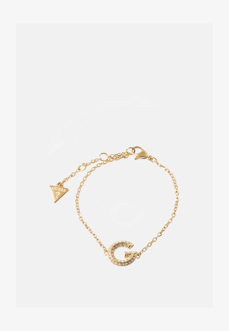 Bracciale in oro con ciondolo a forma di lettera 'G' decorato con strass trasparenti e un'etichetta triangolare 'GUESS'. Texture liscia e design elegante.