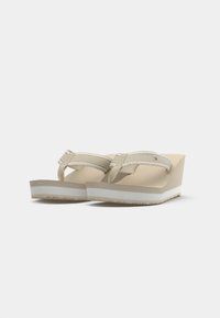 Béžové sandály na klínku s tlustou bílou podrážkou, látkovými pásky a logem. Hladká textura a zaoblený tvar zajišťují stabilitu a pohodlí.