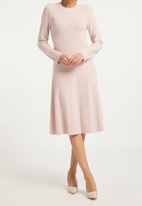 Ljusrosa långärmad klänning med rund halsringning, ribbat mönster, utställd fåll och slätt tyg. Matchad med beige högklackade skor.