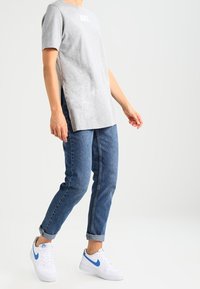 Ljusgrå Nike-t-shirt med korta ärmar, sidofickor, ihopparad med blå denim jeans och vita sneakers med blå accenter.