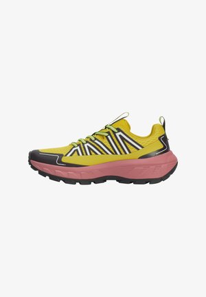 Chaussure de sport jaune et noire avec une tige en mesh texturé, un motif zigzag prononcé, des lacets verts et une semelle intermédiaire épaisse rose.