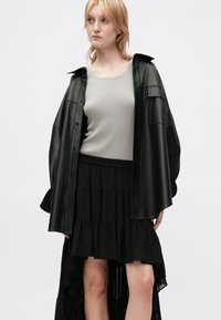 Chemise oversize en cuir noir, top côtelé gris clair, et jupe à volants noirs en couches. Texture lisse, coupe décontractée, avec détails de manches retroussées.
