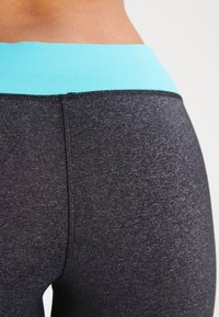 Leggings noirs à finition texturée, avec une ceinture élastique bleu clair. Vue en gros plan mettant en avant les détails des coutures.