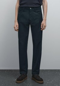 Tmavě zelené chinos kalhoty z bavlny, s klasickým střihem, rovnými nohavicemi, předními kapsami a jedním knoflíkem na zapínání. Texturovaný povrch.