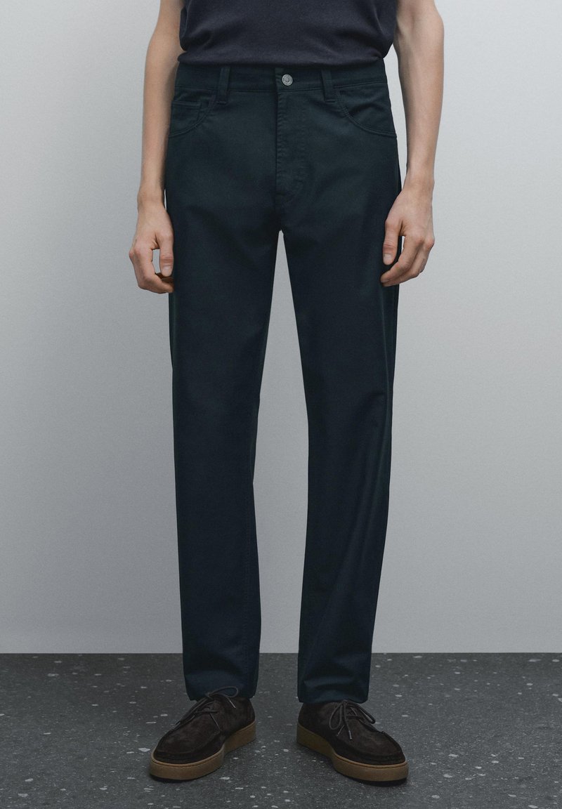 Tmavě zelené chinos kalhoty z bavlny, s klasickým střihem, rovnými nohavicemi, předními kapsami a jedním knoflíkem na zapínání. Texturovaný povrch.