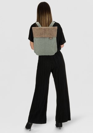 Mochila de tela verde con una solapa superior de ante marrón. Cuenta con correas ajustables y una pequeña etiqueta de la marca en el lateral.
