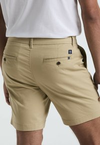 Beige Shorts aus glattem Stoff, mit einer Gesäßtasche und Knopfverschluss, dezentem Logo und taillierter Passform. Der Saum endet auf Oberschenkelhöhe.